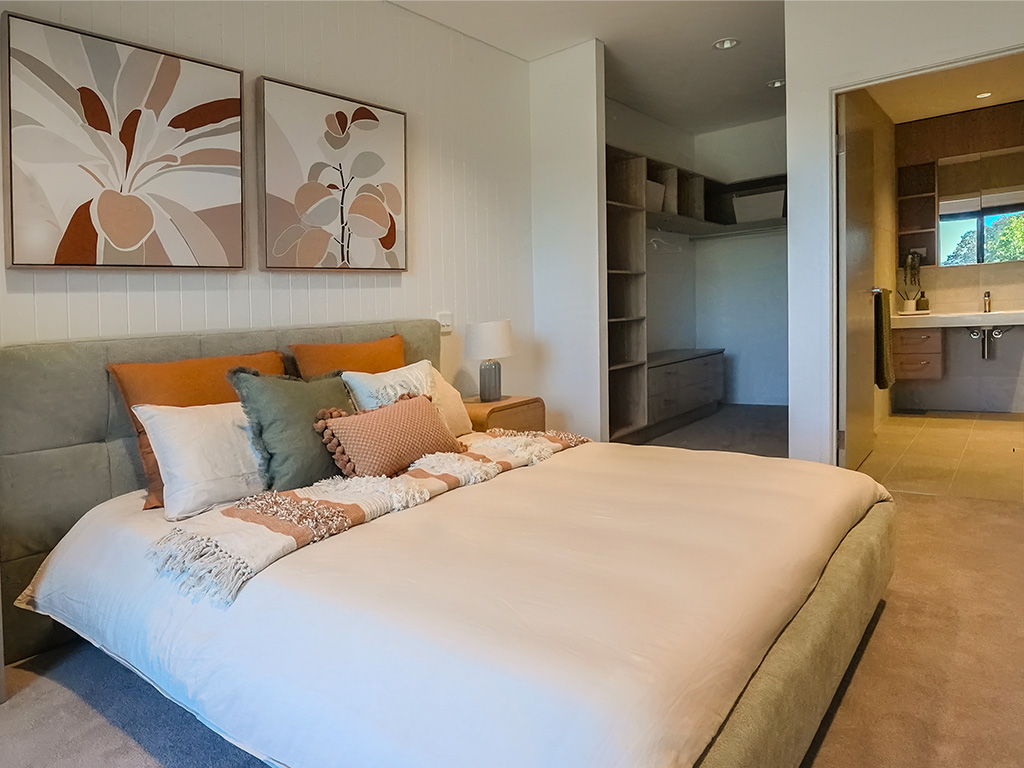furnished main bedroom with ensuite and walk in robe at Assisi apartments showing queen size bed and artwork on wall
