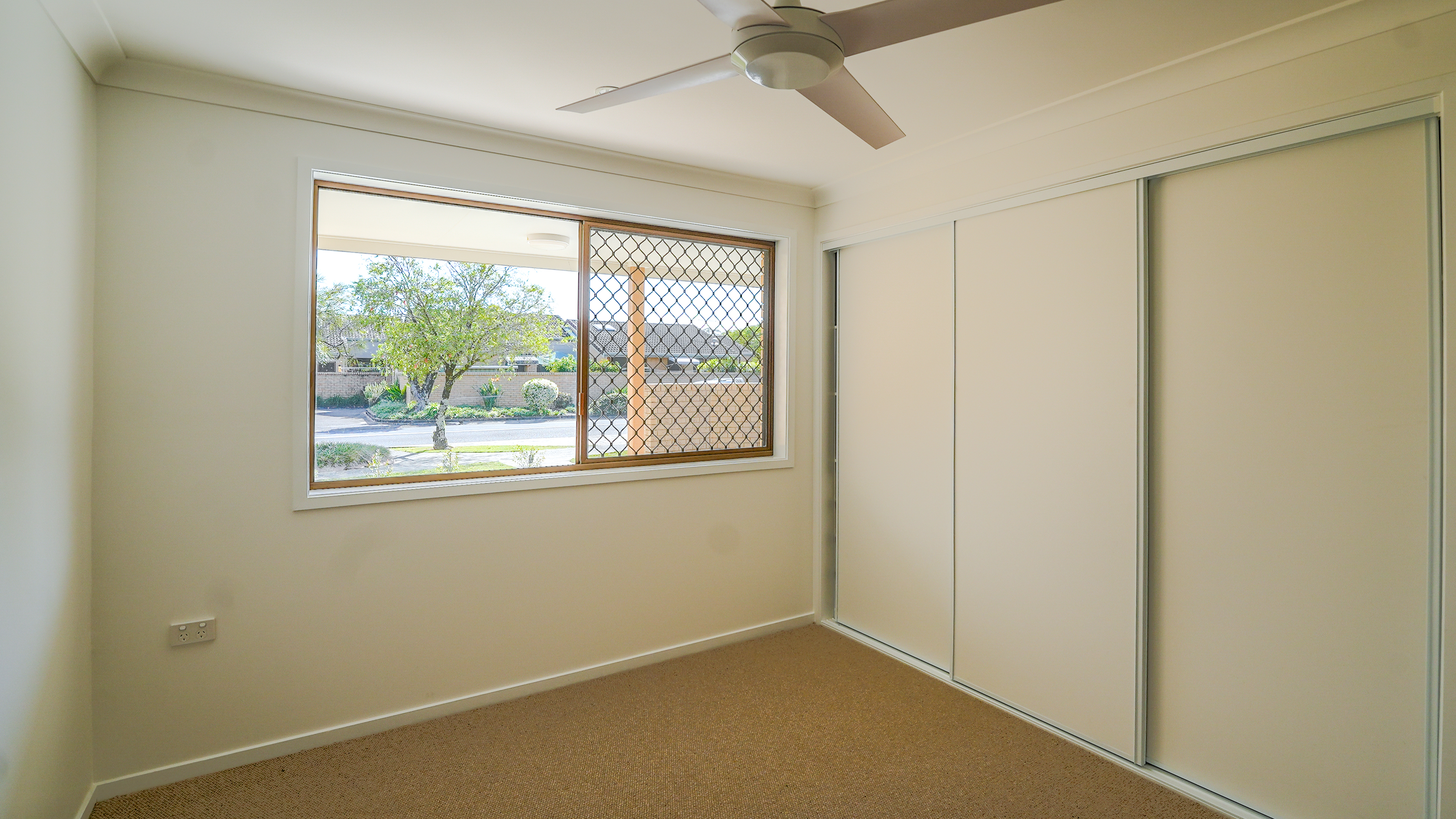 empty bedroom with built in wardrobe, security screen on window and ceiling fan